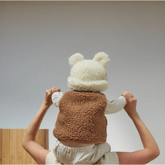 Flauschiger Teddybär mit weißem Hut und braunem Körper in menschlichen Händen