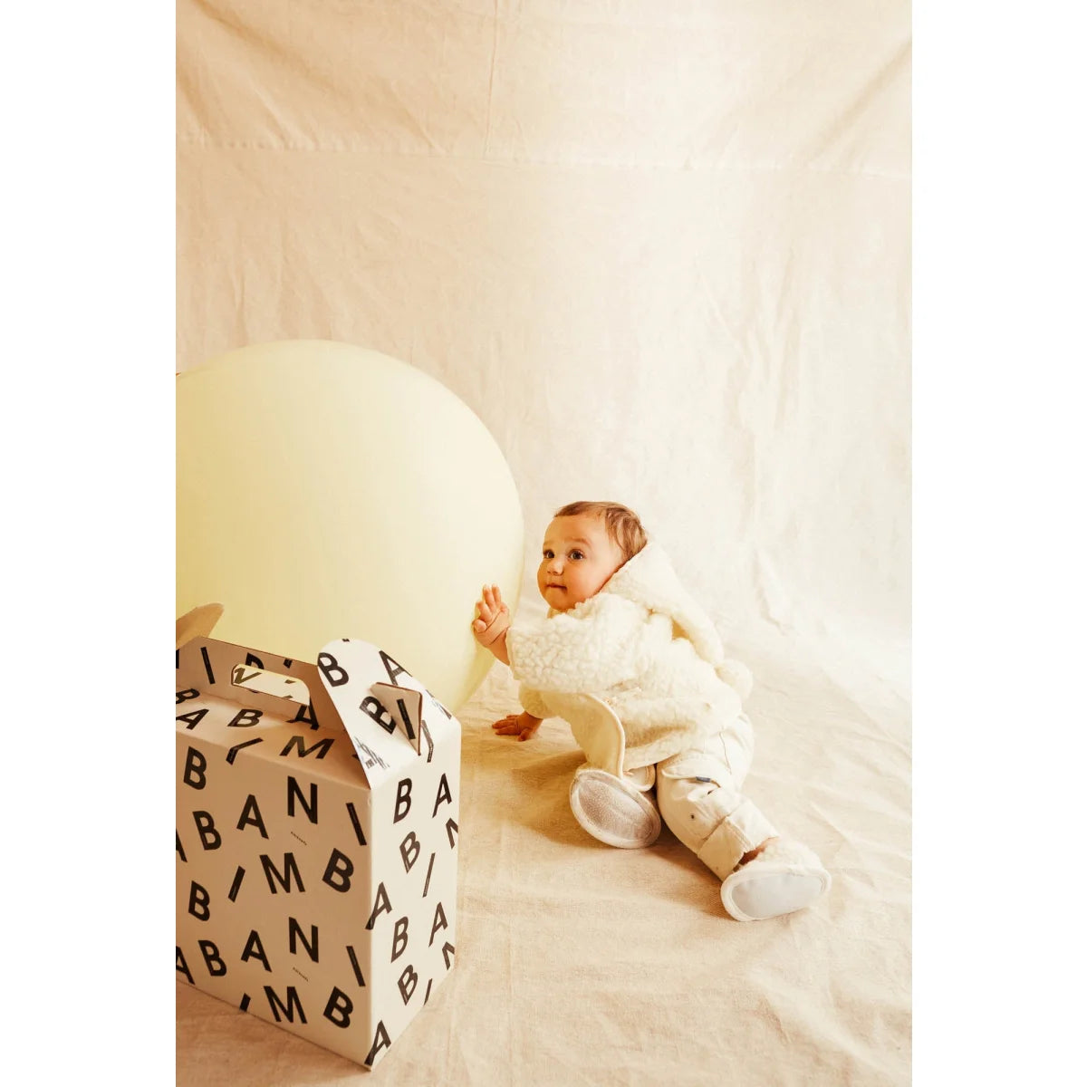 Baby sitzt auf dem Boden neben einem Geschenk mit Buchstabenmustern