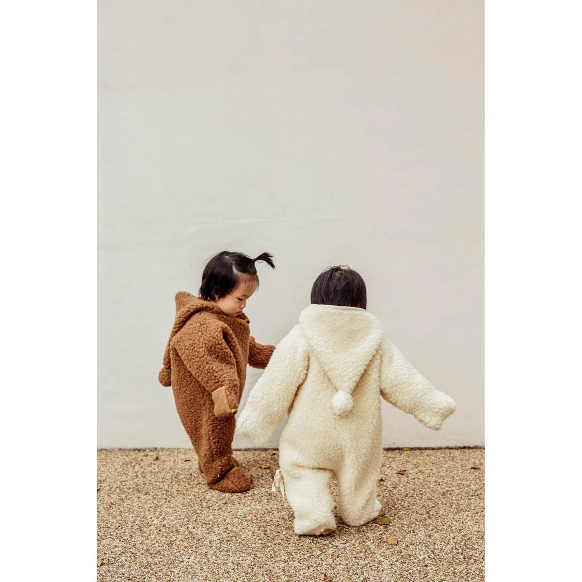 Zwei Kleinkinder in flauschigen Tier-Overalls stehen zusammen im Merino Snugglesuit