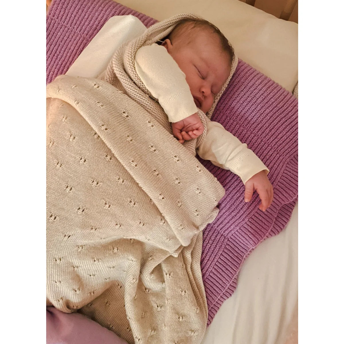 Schlafendes Neugeborenes in cremefarbener Merino Strickdecke auf lila Oberfläche