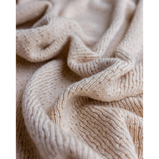 Cremefarbener Strickstoff mit strukturiertem Rippenmuster und Falten von Merino Strickdecke Dora