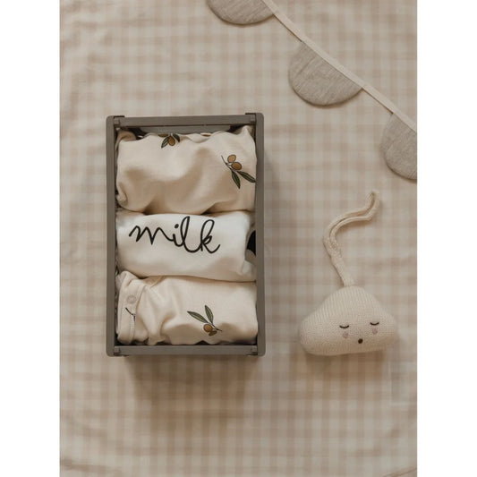 Holzkiste mit gefalteter Babykleidung, mit einem Artikel beschriftet MILK