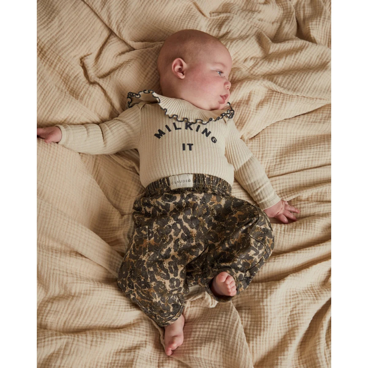 Creamfarbener gerippter strick langarm bodysuit mit schwarzem milking it schriftzug und gerafftem kragen zu oliv-beigem leopardenprint hose