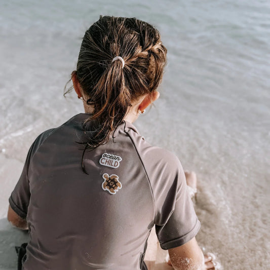 Dunkelgraues kurzärmeliges rashguard aus mückenschutz ocean child edition mit logo und schildkrötenpatch auf der rückseite