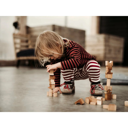 Ein kind in rot-weiß gestreifter nachhaltige babykleidung schweiz baut einen turm mit ökologischem spielzeug naturelle holzklötze geschenke für neugeborene