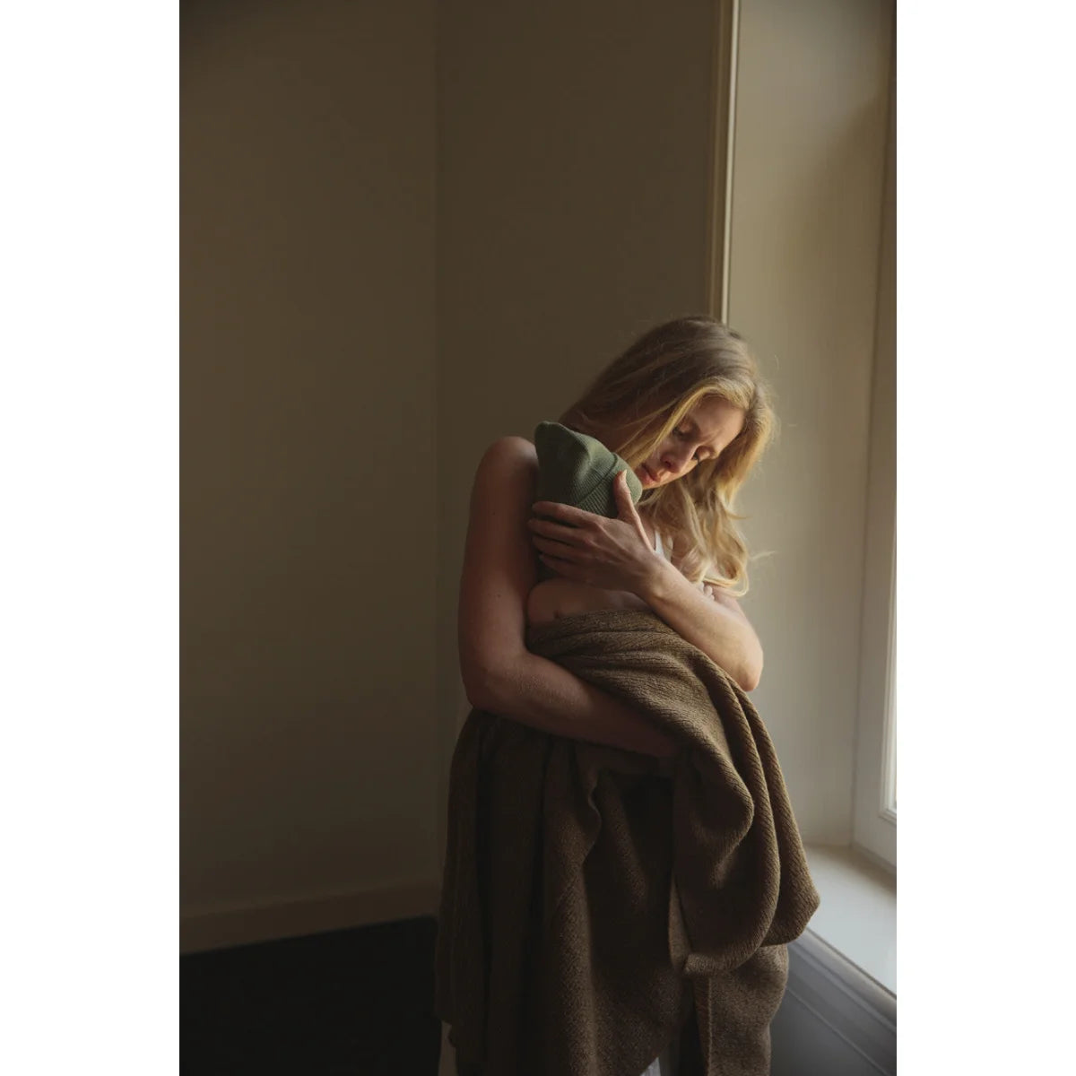 Frau in einer Decke am Fenster mit dem Beanie Fonzie aus ökologischer Kinderbekleidung