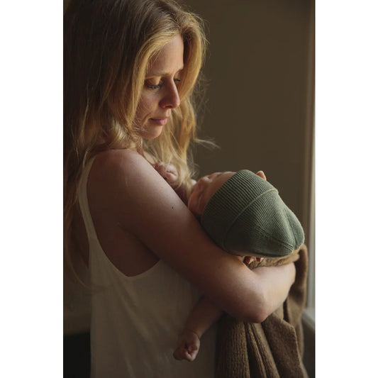 Frau hält Neugeborenes in grünem Blanket mit Beanie Fonzie für ökologische Kinderbekleidung