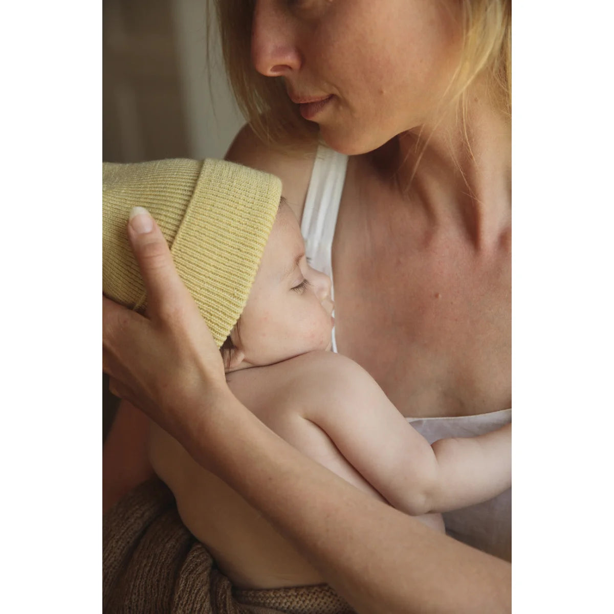 Eine Frau stillt ein Baby in einer gelben Decke, passend zur Neugeborenenmütze