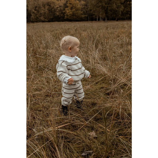 Kleinkind im gestreiften Outfit steht in hohem Gras mit Oversize Knit Pullover