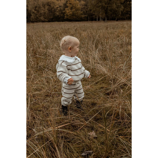 Kleinkind im gestreiften Outfit steht in hohem Gras mit Oversize Knit Pullover
