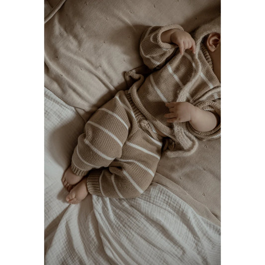 Baby in gestreiftem Strick-Overall auf Bettwäsche liegend, Oversize Knit Pullover Stripe