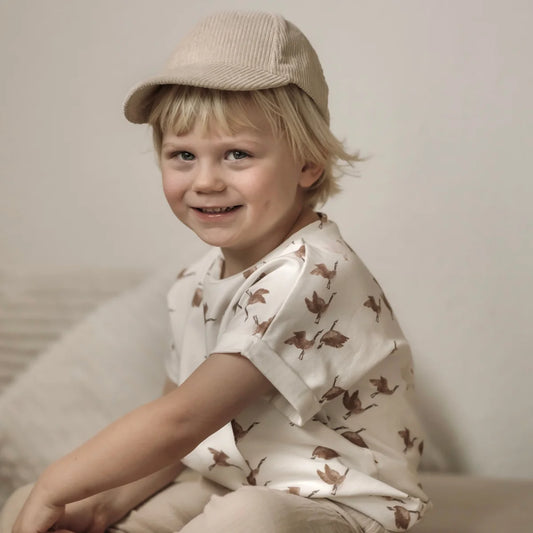 Lächelndes Kind in einer oversized Gänsemuster-Bluse und -Mütze