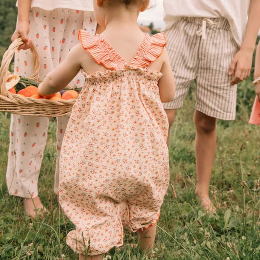 Kind im pfirsichfarbenen Búho Baby Picnic Jumpsuit in Coral mit Blumenmuster