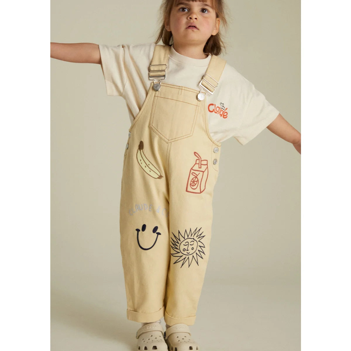 Ein Kind in illustrierten Latzhosen aus dem Piper Breakfast Dungaree Produkt