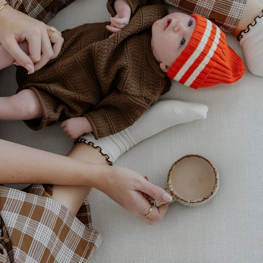 Baby in orange gestreiftem Hut neben Postpartum Collagen Schokoladengetränk im Glas