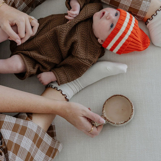 Baby in orange gestreiftem Hut neben Postpartum Collagen Schokoladengetränk im Glas