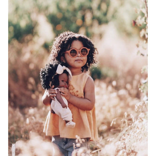 Junges Mädchen mit lockigem Haar, Sonnenbrille und Puppe Loreta in den Händen