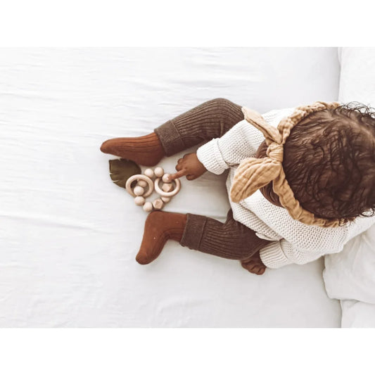 Baby auf weißer Unterlage im Strickpullover und braunen Hosen von Rassel Leaves