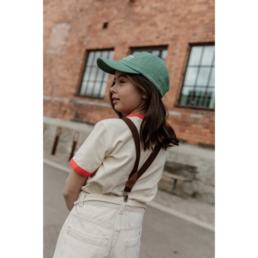 Mädchen mit grünem Baseballcap und Hosenträgern im Retro V Braces Design