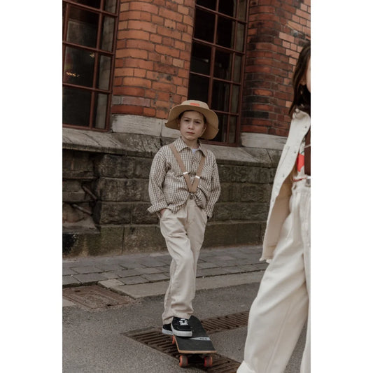 Junge auf Skateboard mit Retro V-Trägern in Sandbraun
