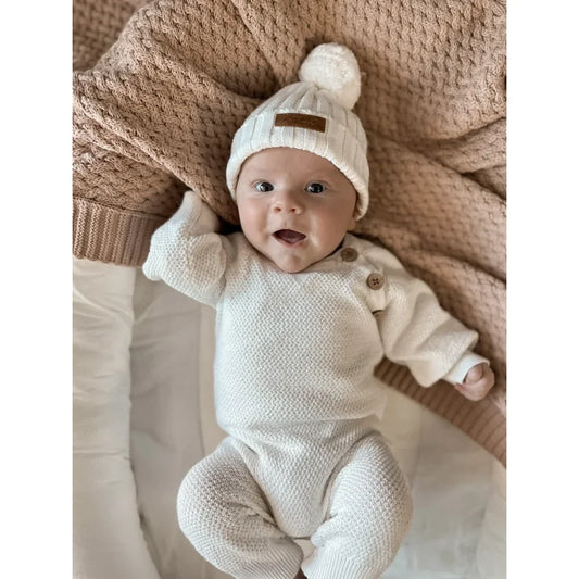 Baby in a weißen Strick-Outfit mit Bommelmütze, präsentiert in Ribbed Beanie | Milk