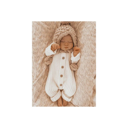 Schlafendes Neugeborenes im gestrickten weißen Overall und beigem Hut in Milchfarbe
