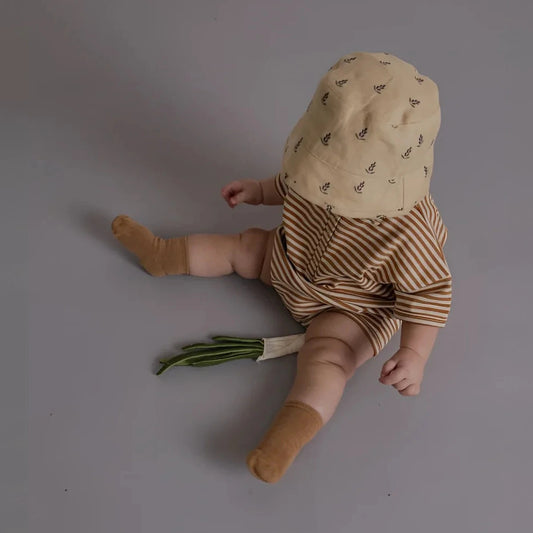 Baby im Organic Zoo Romper in Copper Stripes Beach, braun-beige gestreift, mit beigem Bucket Hat mit Blättermuster