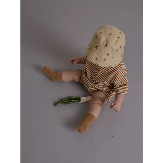 Ein baby trägt einen romper copper stripes beach mit gestreiften braun-beigen shorts und beigem bucket-hut mit blättermuster