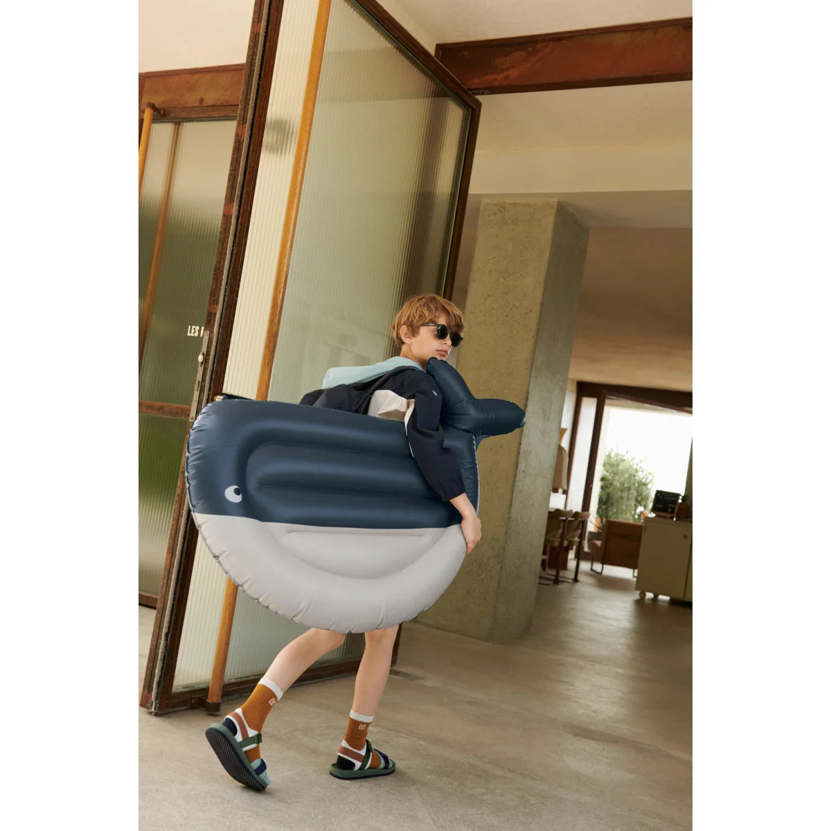 Kind trägt aufblasbaren Wal, während er Sandalen Monty in grün trägt