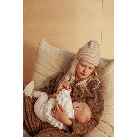 Frau wiegt Baby auf Kissen, getragen in Schaffell Booties in Milchfarbe