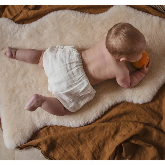 Baby auf einem Teppich mit einer Orange, Schaffell Snuggler Leopard Peanut