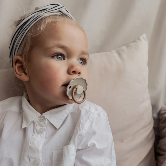 Baby mit blonden Haaren in weißem Shirt und gestreiftem Kopftuch mit Schnuller