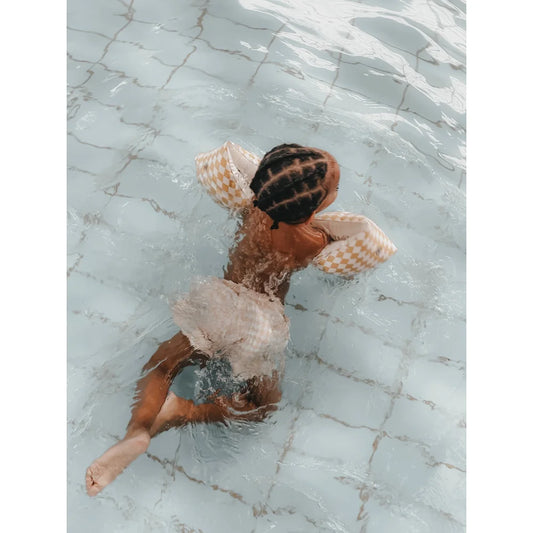 Kind schwimmt mit Schwimmflügel in Schimmelflieder-Diamantmuster