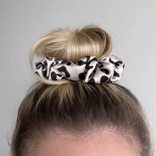 Chouchou « Fable » Everydayscrunchie imprimé vache noir et blanc sur un chignon châtain clair