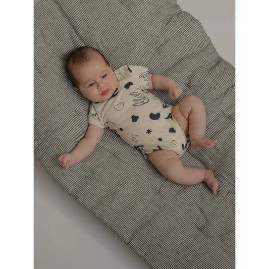 Baby in einem gemusterten Kurzarm-Bodysuit in Capri-Farbe