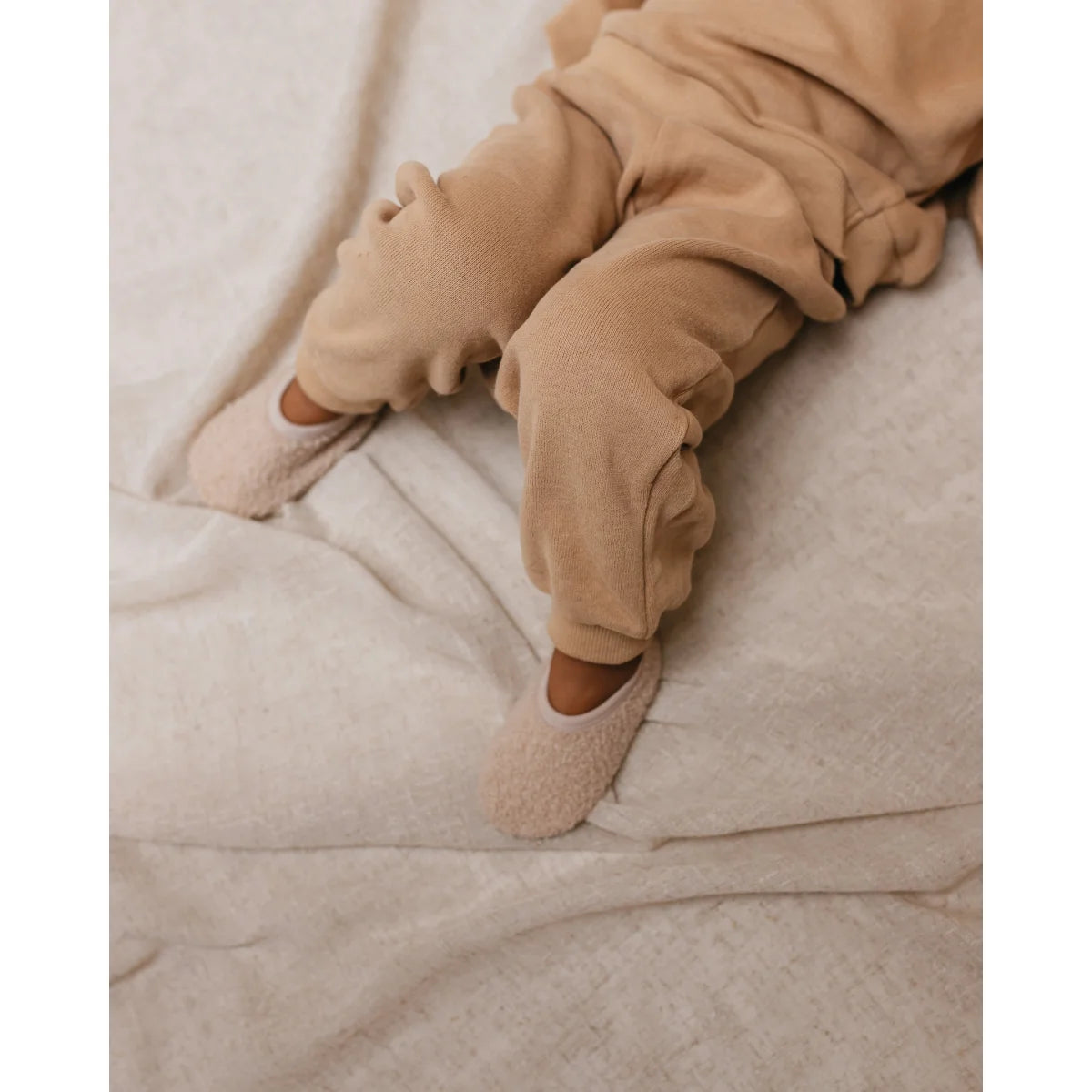 Babybeine in beigem Onesie aus weicher Baumwolle auf hellem Stoff von Ertha Slogges