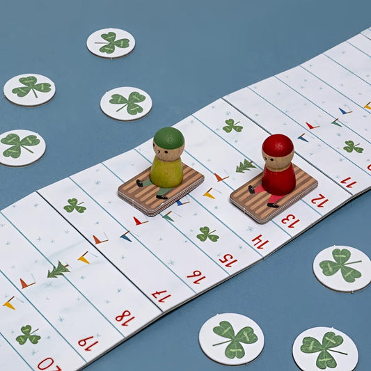 Snow Race Tiny Game: Holzstecker mit grünen und roten Hüten auf gestreiften Kartonbooten