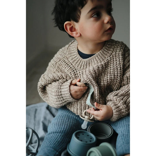 Junges Kind in einem chunky Strickpullover mit einer Teekanne im Stapelturm Forest