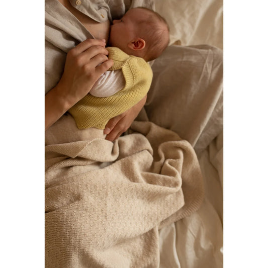 Neugeborenes Baby im gelben Pullover auf weichem Bettzeug in jemandes Armen