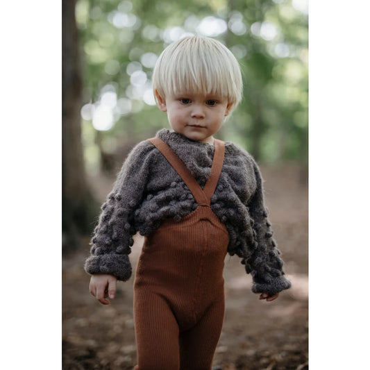 Junge in braunem Strick-Overall und flauschigem grauen Pullover von Cinnamon
