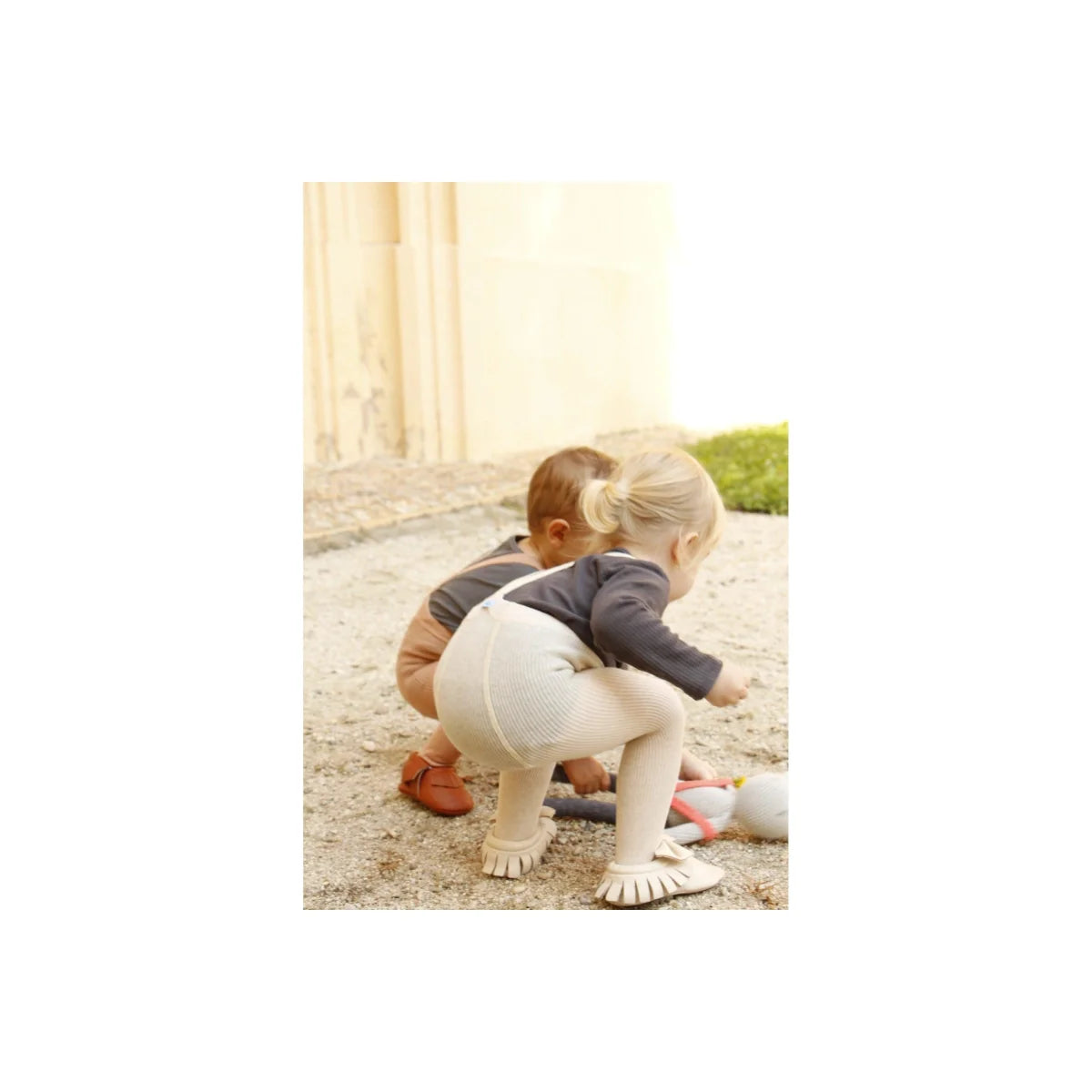 Kleinkind in weißem Bodysuit mit Bären-Design auf dem Rücken und Strumpfhose mit Träger