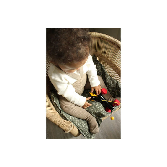 Junges Kind mit lockigem Haar spielt in einem Korbsessel mit bunten Spielzeugen