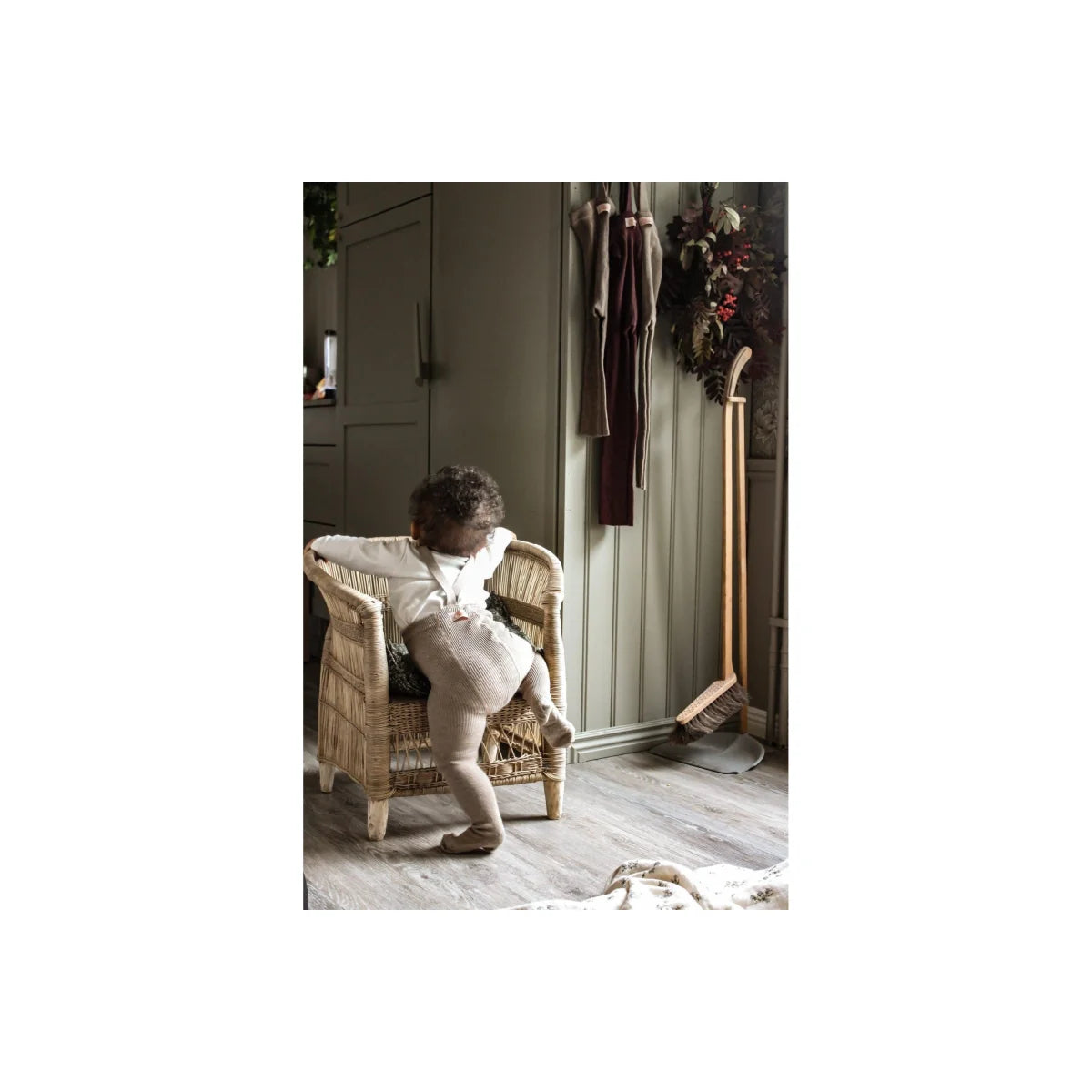 Kleinkind im Windel klettert auf einen Korbstuhl, umgeben von Strumpfhose mit Träger