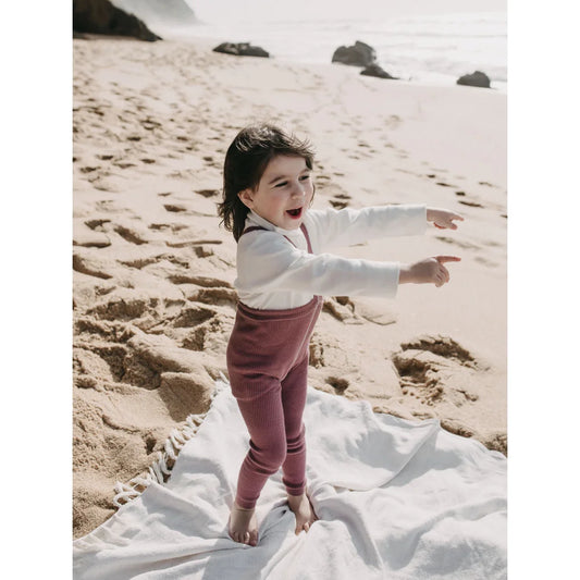 Junger Junge am Strand auf weißem Tuch mit ausgebreiteten Armen in Strumpfhose