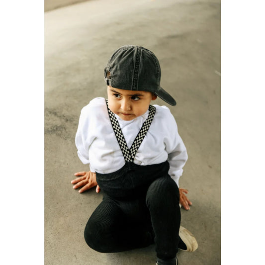 Junger Junge mit Cap, weißem Shirt und dunklen Hosen, kauert auf dem Boden