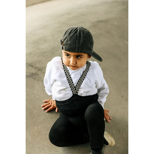 Junger Junge mit Cap, weißem Shirt und dunklen Hosen, kauert auf dem Boden