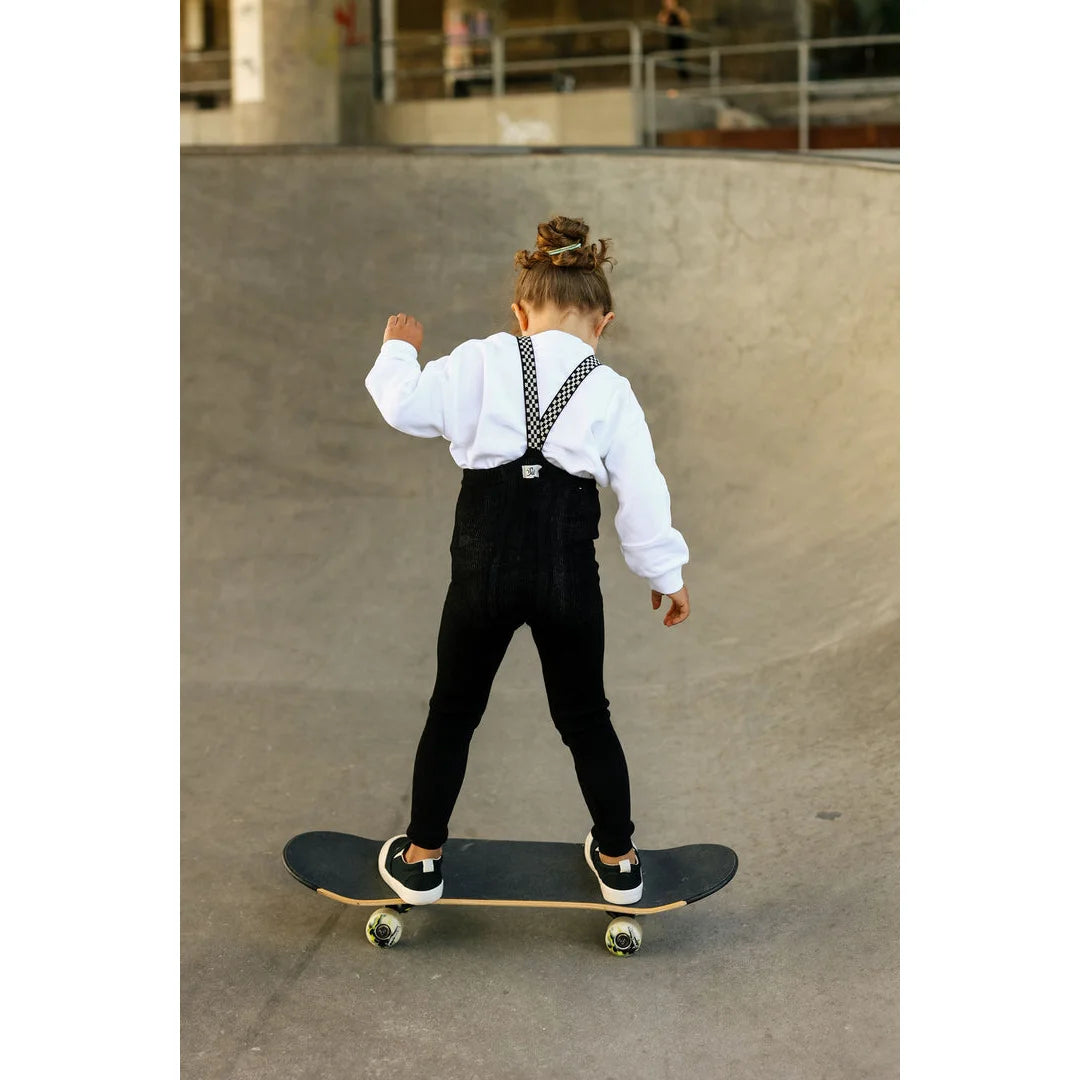 Junger Skateboarder in weißem Shirt und schwarzen Overalls auf einem Skateboard