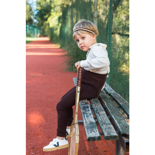 Kind sitzt mit Tennisschläger und trägt Schokoladenbraune gestreifte Strumpfhose