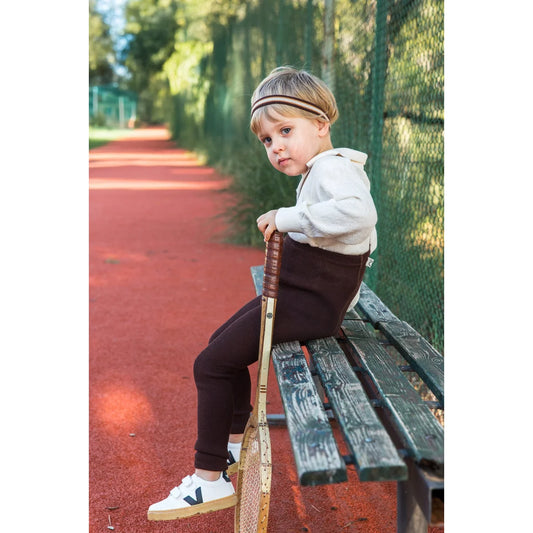 Kind sitzt mit Tennisschläger und trägt Schokoladenbraune gestreifte Strumpfhose