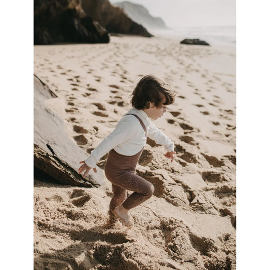 Kind, das an einem Sandstrand läuft, trägt Strumpfhose mit Träger Footless | Granola